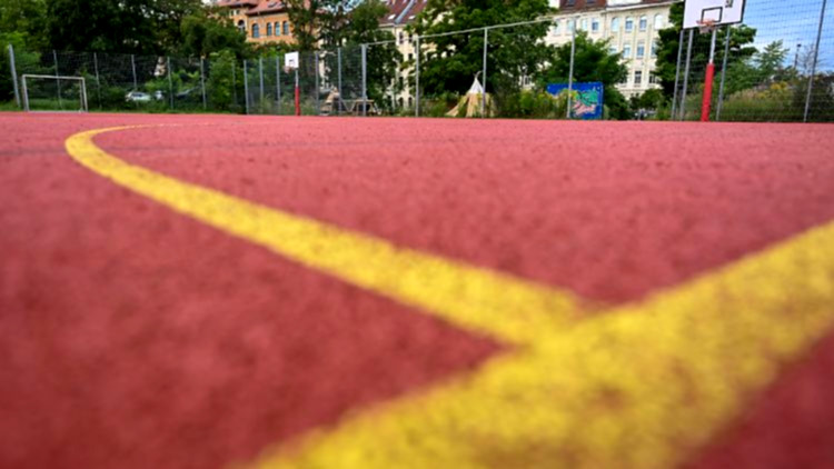 Kinder spielen Basketball auf Schulhof.